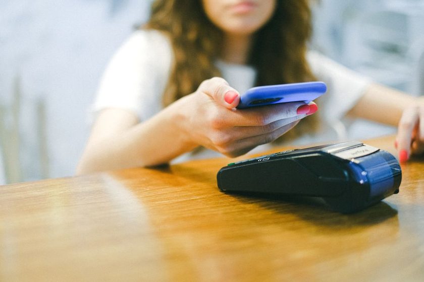 Mulher aproxima o celular de uma maquininha de cartão para autorizar um pagamento por aproximação.